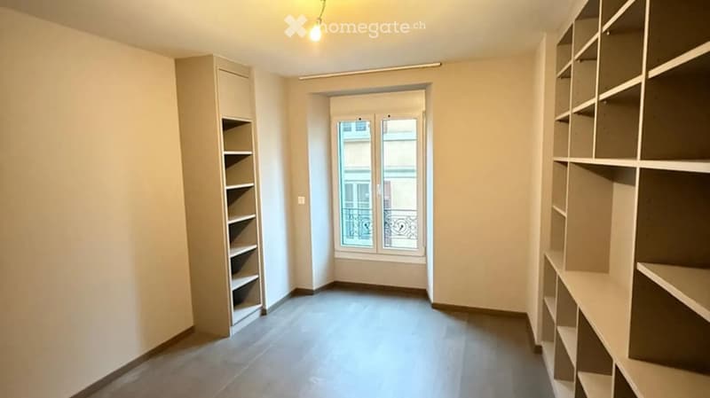 Empty room with built-in shelving units on both sides, a large window with a view, and a door leading to a balcony.