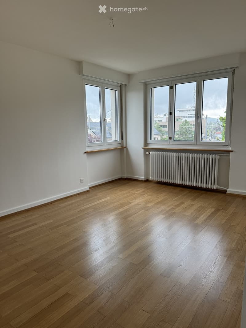 Empty room with wooden flooring, large windows, and a radiator under one window.