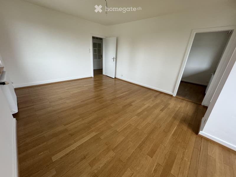 Empty room with wooden flooring and white walls, featuring two open doorways leading to adjacent spaces.