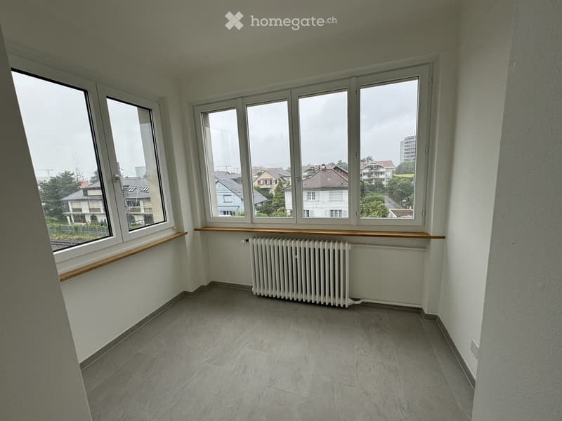 Empty room with tiled floor, white walls, large windows with wooden sills, and a radiator under the windows.