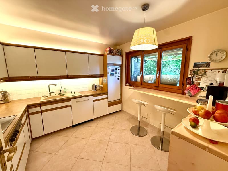 Bright kitchen with white cabinets, wooden trim, and a central island with bar stools. Features a sink, refrigerator, and various appliances.