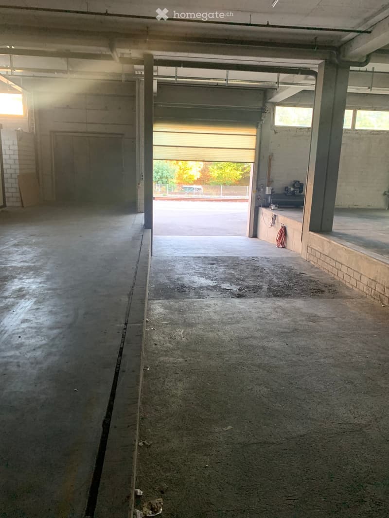 Empty garage with concrete floor, large garage door, and minimal equipment visible.