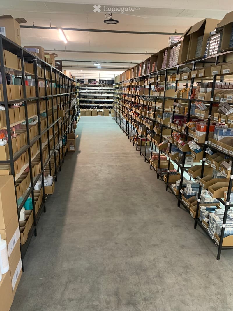 A storage area with rows of metal shelving units filled with cardboard boxes and various items, concrete floor, industrial lighting.