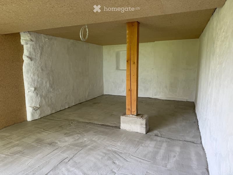 Empty room with bare walls and a concrete floor, featuring a wooden support column and a small window.