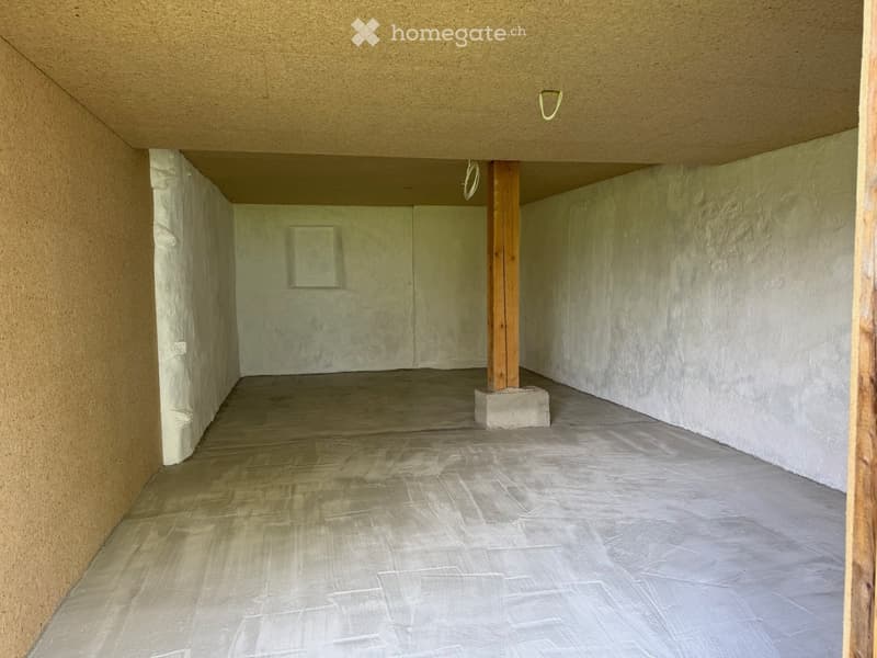 Empty room with bare walls and a concrete floor, featuring a wooden support beam and a small concrete block in the center.