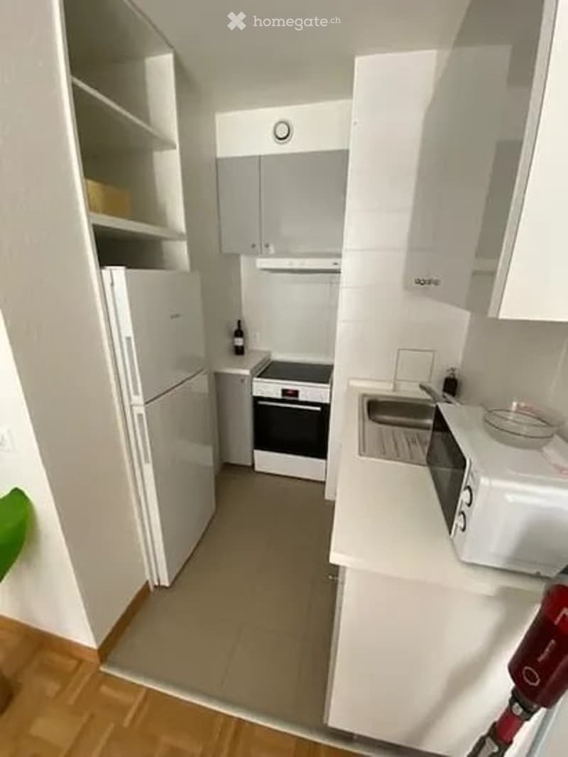 Modern, compact kitchen with white cabinets, stainless steel appliances, and a small dining area. Features include a refrigerator, oven, microwave, sink, and a few decorative items.