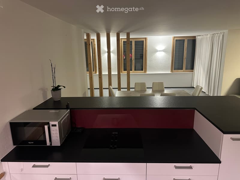 Modern kitchen with white cabinets, black countertops, microwave, and a small dining area with chairs and a table.