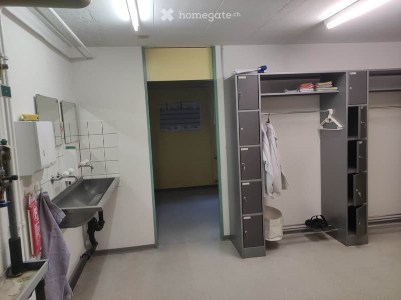A locker room with a sink, mirrors, a locker cabinet, and various personal items like towels and shoes.