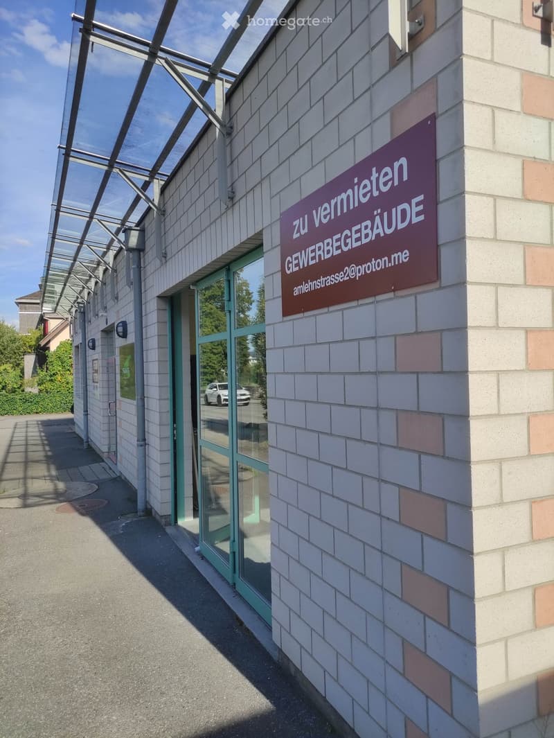 Exterior view of a building with a sign reading "zu vermieten GEWERBEGEBÄUDE" and an email address, featuring a glass entrance and tiled facade.