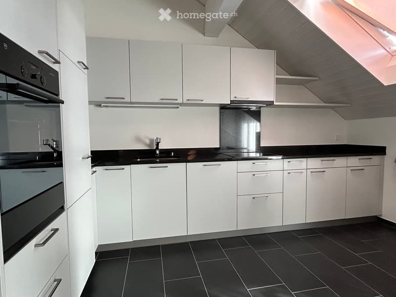 Modern kitchen with white cabinets, black countertops, and dark tiled flooring. Features an oven, sink, and faucet.