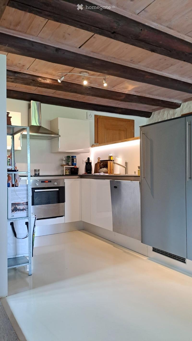 Modern kitchen with white cabinets, stainless steel appliances, and exposed wooden beams on the ceiling. Features include a refrigerator, oven, dishwasher, and a range hood.