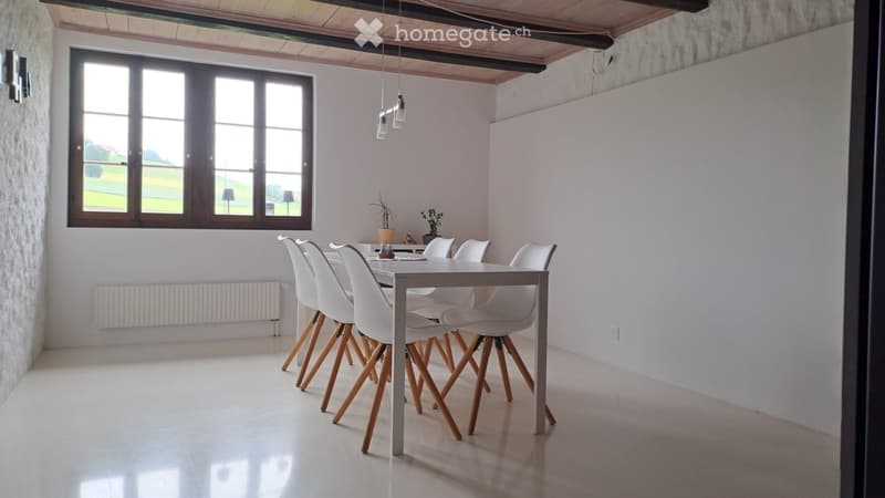 Bright dining room with white walls, large window, modern dining table and chairs, and pendant lighting.