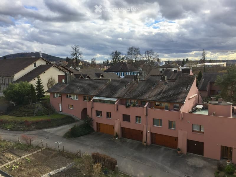A two-story pink house with multiple garage doors, windows, and a small balcony area with outdoor furniture.