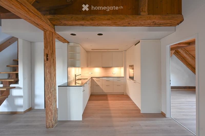 Modern kitchen with white cabinets, a central island, and a sleek sink area. The space features wooden flooring and exposed wooden beams on the ceiling.