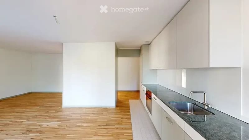 Empty kitchen with white cabinets, wooden flooring, and a stainless steel sink. No furniture or appliances are present.