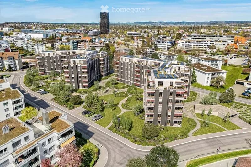 Aerial view of a modern residential complex with multiple apartment buildings, green spaces, and parking areas.
