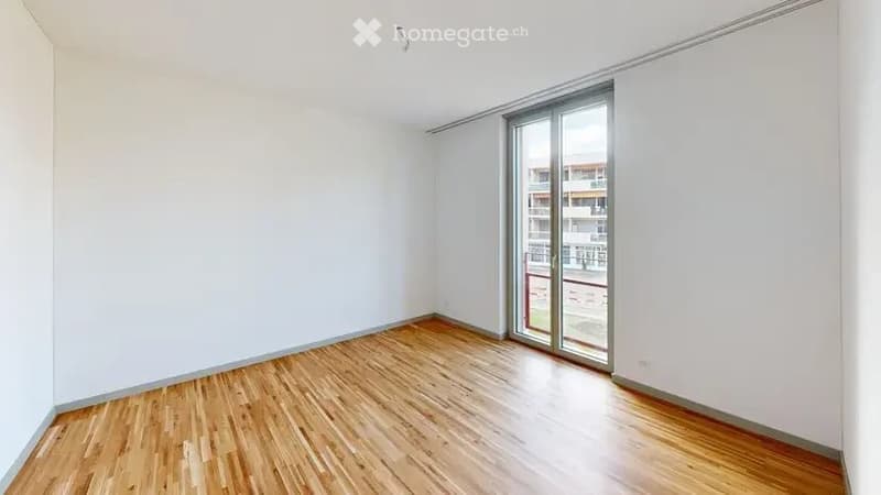 Empty room with wooden flooring, white walls, and large sliding glass door leading to a balcony.