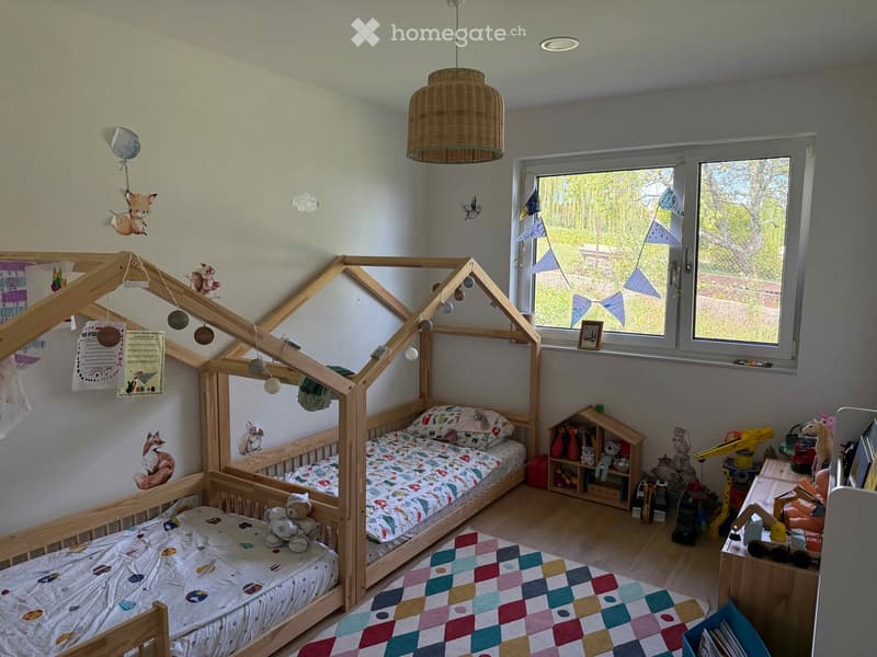 A brightly decorated children's bedroom with a wooden playhouse bed, colorful bedding, toys, and a hanging basket lamp.