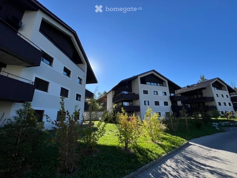 Modern apartment complex with white and dark wood facades, multiple balconies, and surrounding greenery.