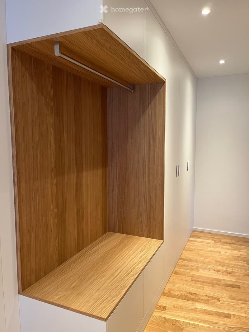 Empty hallway with wooden shelves and white walls, featuring recessed lighting and a wooden floor.