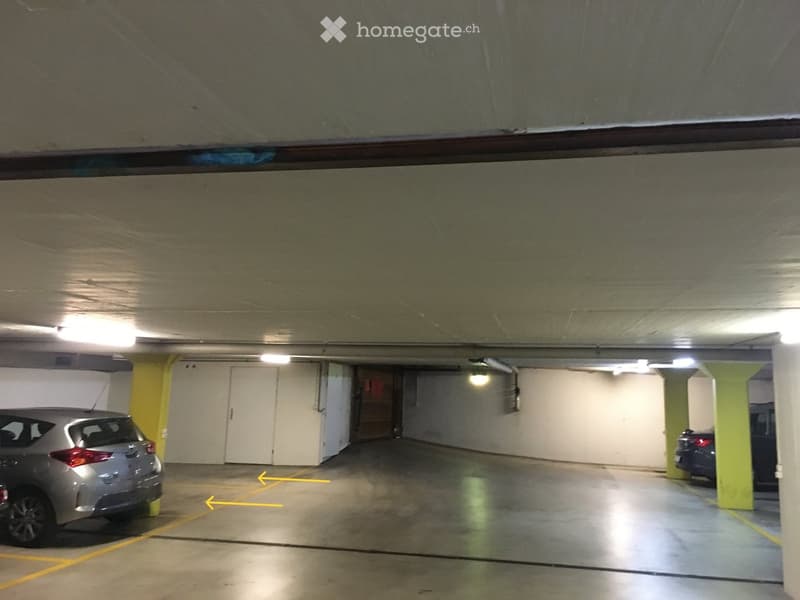 Underground parking area with concrete floors, white walls, yellow pillars, and two parked cars.