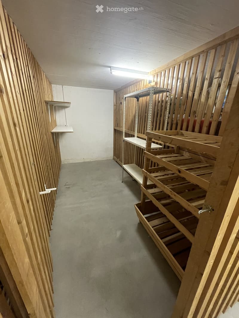 Empty room with unfinished wooden walls and shelves, concrete floor, and exposed ceiling beams.