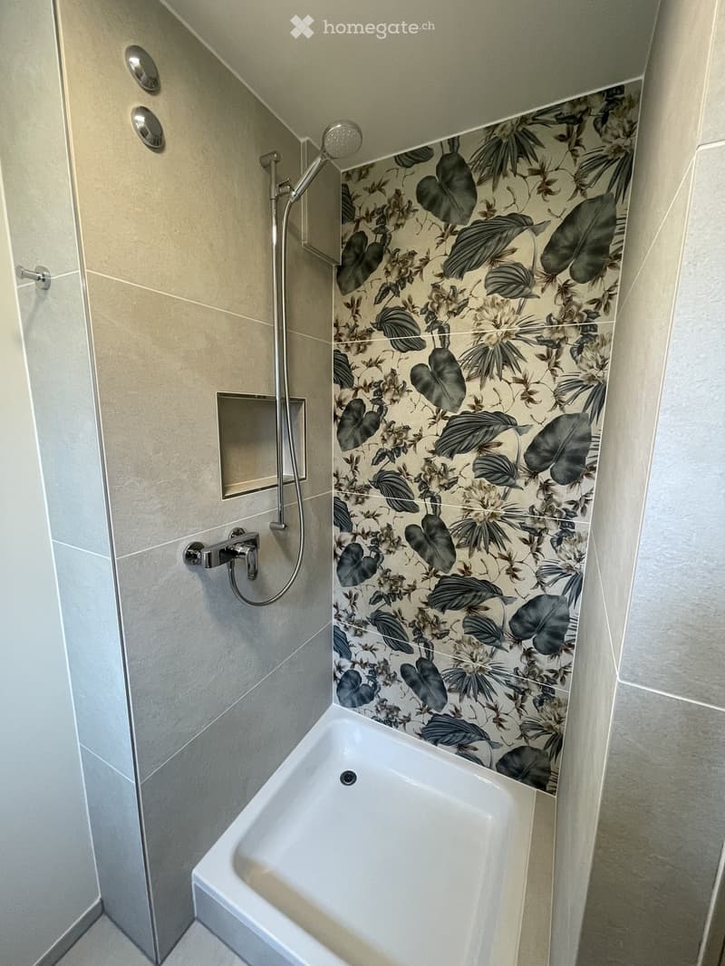Modern bathroom with a bathtub, floral-patterned tiles, and a handheld showerhead.