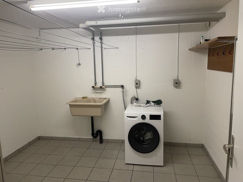 A small bathroom with a washing machine, a sink, tiled floor, and white walls.