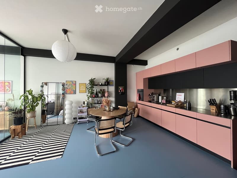 Modern kitchen with pink cabinets, stainless steel appliances, a round dining table with four chairs, pendant light, and decorative plants.
