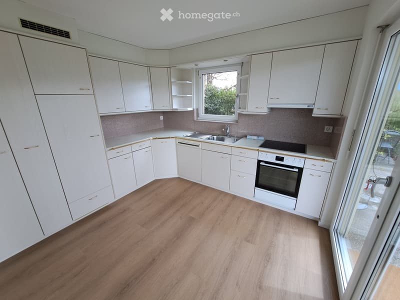 Modern kitchen with white cabinets, wooden flooring, and stainless steel appliances including a sink, stove, and oven.