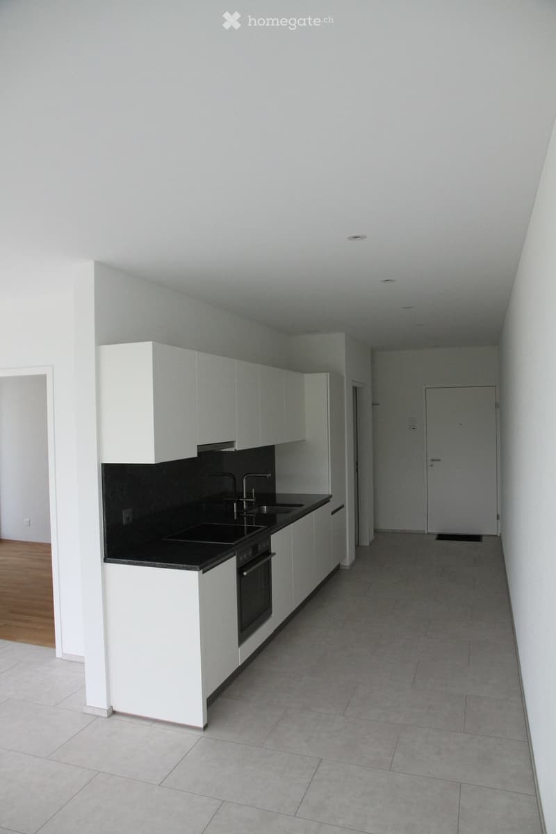 Modern kitchen with white cabinets, black countertop, sink, and oven. The space is clean and well-lit with tiled flooring.