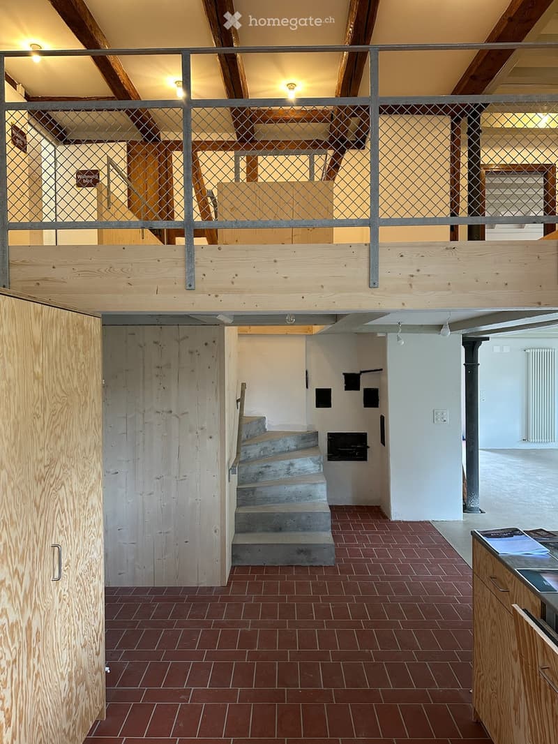 Open hallway with exposed wooden beams, metal railing, brick floor, and a staircase leading to an upper level.