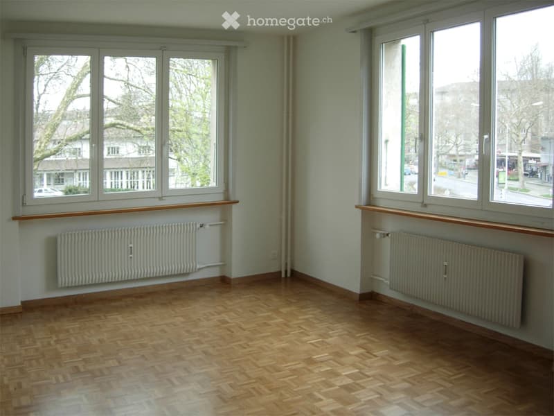 Empty room with wooden flooring, large windows, radiators, and wooden window sills.