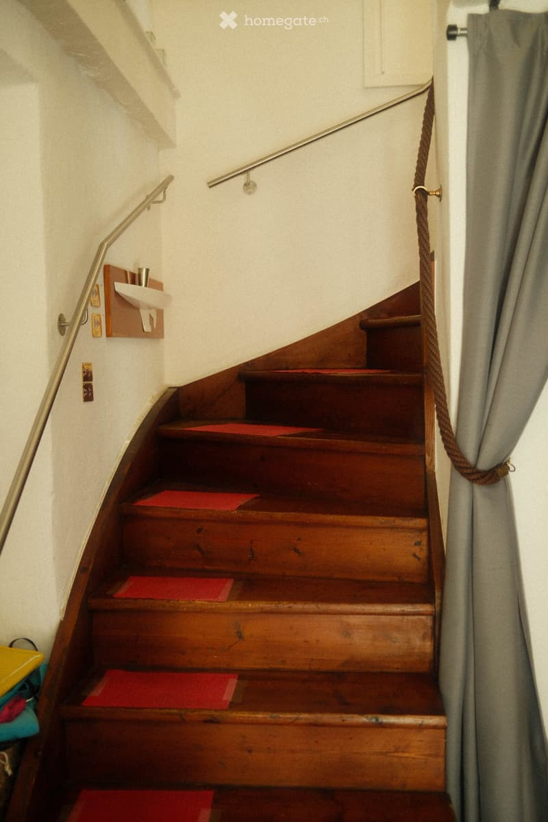 Wooden staircase with red runners, metal handrails, and a small shelf with a sink and decorative items on the wall.