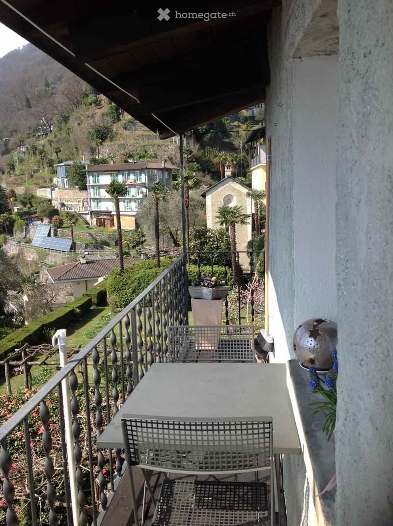 Balcony with a table and chairs, overlooking a scenic hillside with houses and trees.