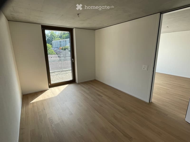 Empty room with light wooden flooring, white walls, and a large sliding glass door leading to a balcony area.