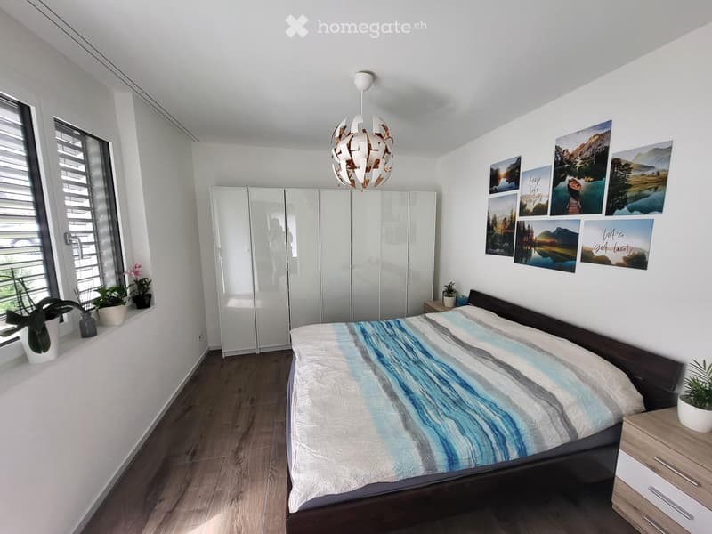 Modern bedroom with a large bed, a wardrobe, nightstand, potted plants, and decorative picture frames on the wall.