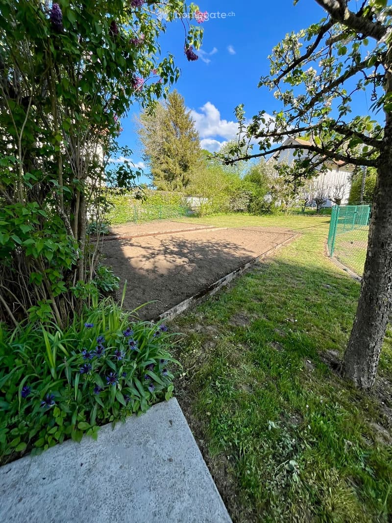 Garden path lined with grass, flowers, and trees leading to a house in the background.