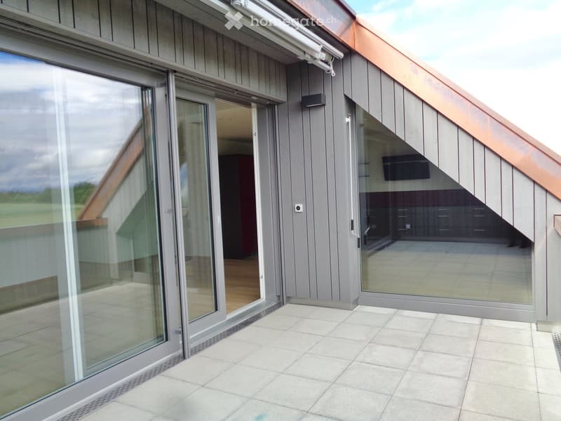 Modern balcony with large glass sliding doors, tiled floor, and a view of the surrounding landscape.