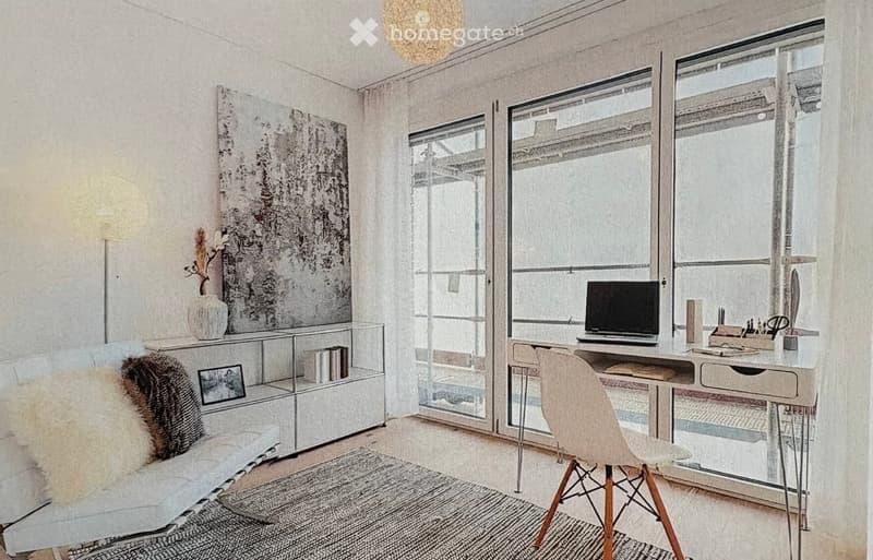 Modern, well-lit room with a desk, laptop, chair, and a cozy seating area with a white chair and throw blanket. Large windows provide natural light, and decorative items like a vase and artwork enhance the space.