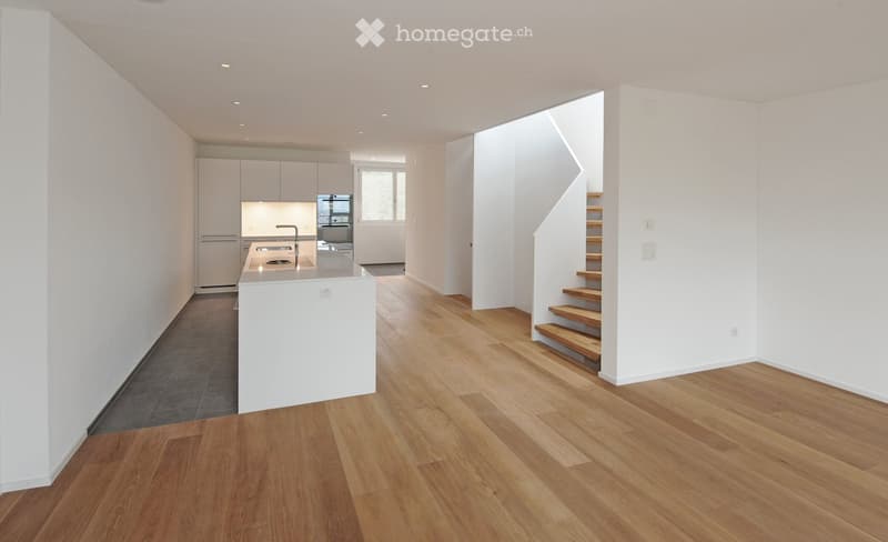 Open-concept kitchen and living area with light wood flooring, white cabinets, and a central island. A staircase leads to an upper level.