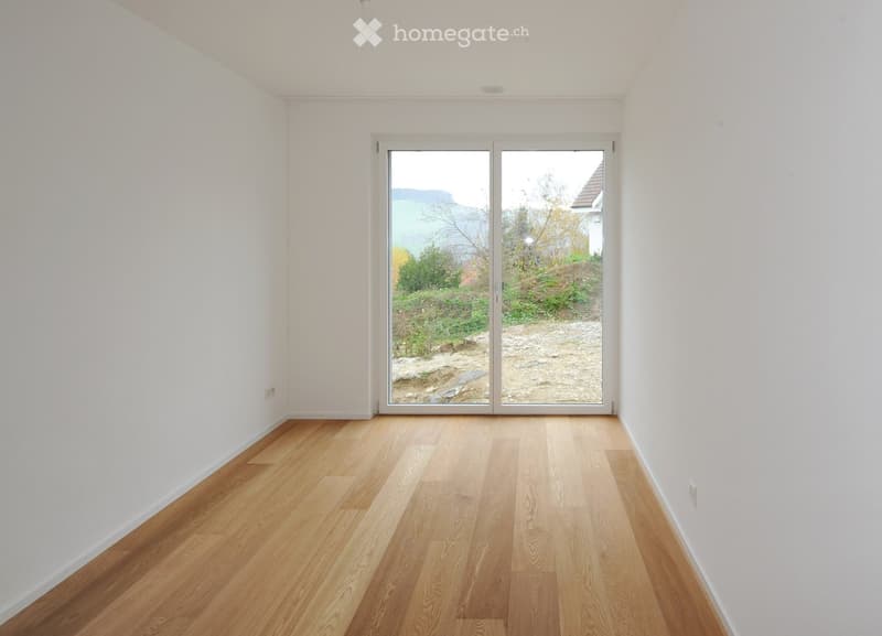 Empty room with light wooden flooring and white walls, featuring a large sliding glass door that opens to an outdoor area.