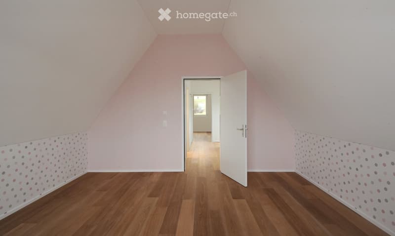 Empty room with wooden flooring, light pink walls, and a white door leading to another space. The walls feature a decorative border with colorful polka dots.