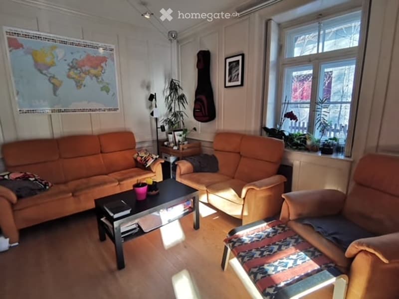Living room with orange sofas, coffee table, armchair, guitar on wall, world map, and plants near window.