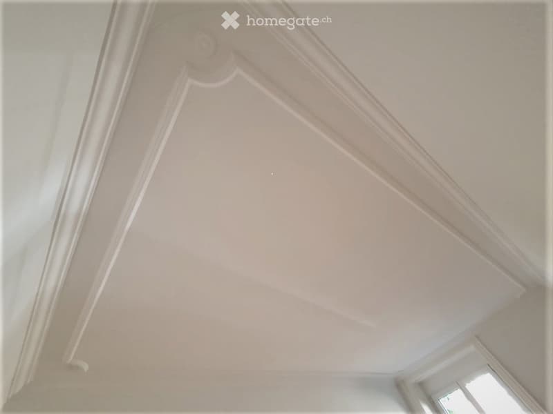 Empty room with a decorative ceiling featuring crown molding and a light fixture, visible through an open doorway.