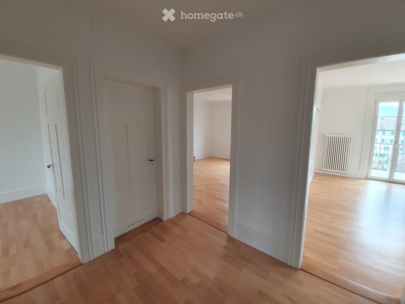 Empty room with wooden flooring, white walls, and multiple doors leading to other spaces.