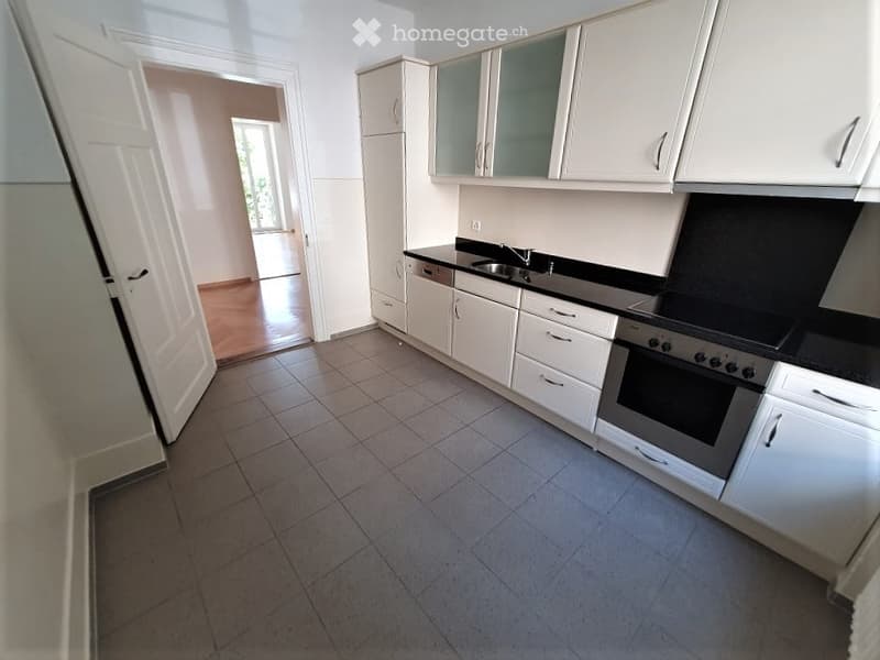 Modern kitchen with white cabinets, black countertops, and stainless steel appliances including an oven and dishwasher. The floor is tiled, and there is a visible doorway leading to another room.