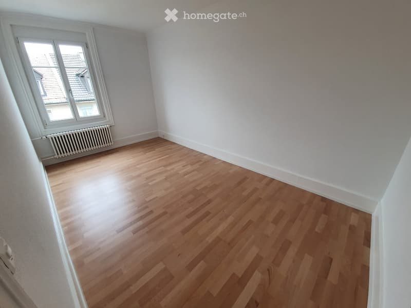 Empty room with wooden flooring, white walls, and a window with a radiator below it.