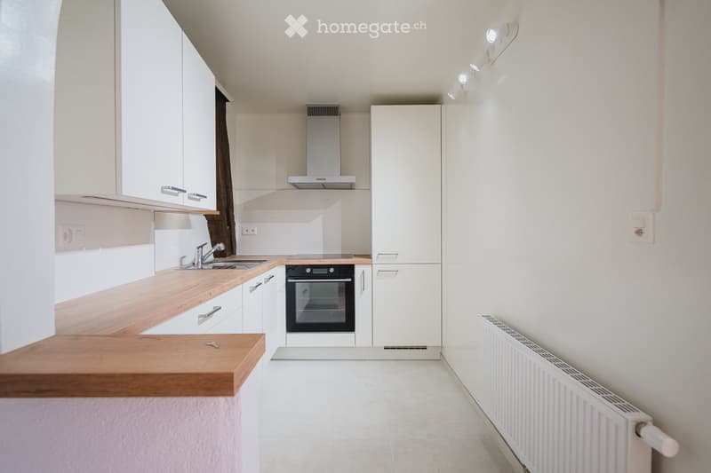 Modern kitchen with white cabinets, wooden countertops, stainless steel sink, oven, and built-in range hood.