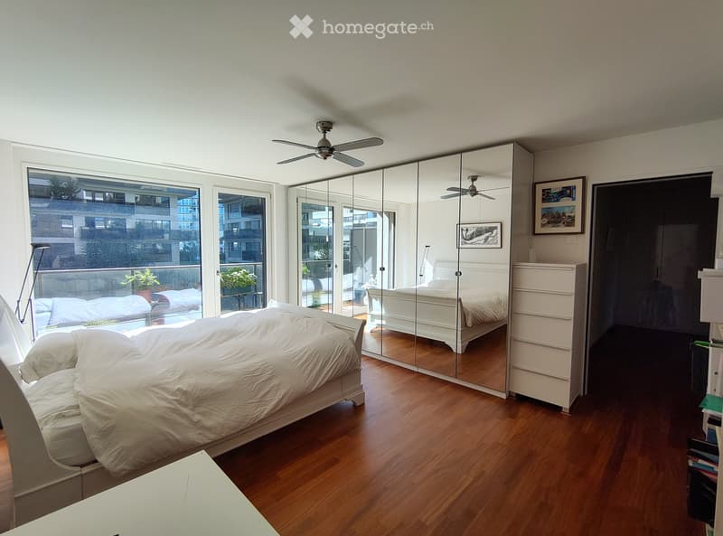 Spacious bedroom with wooden flooring, large mirrored closet, two beds, nightstands, and a balcony with outdoor plants.